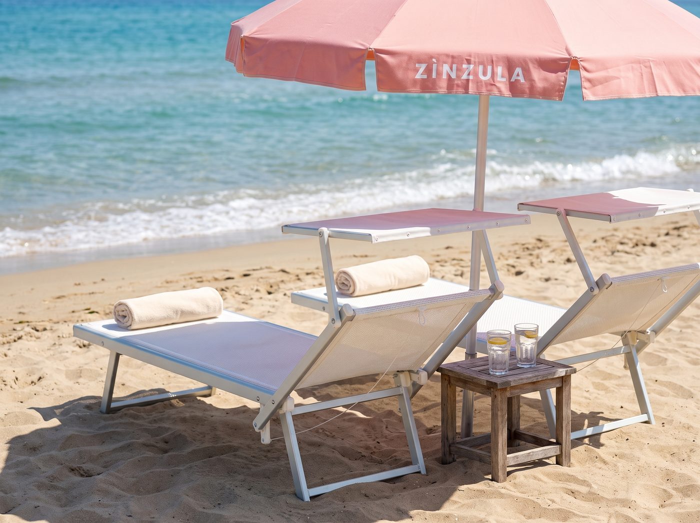 Two sunbeds under a Zinzula umbrella at the shoreline